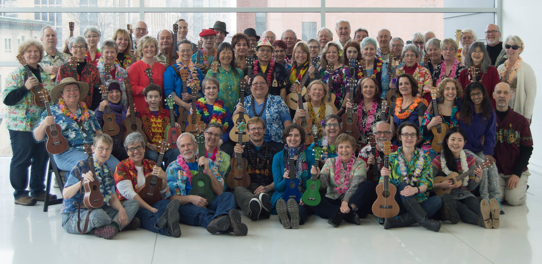 A large group of people wearing colorful Hawaiian shirts, many holding ukuleles.