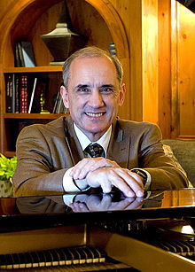 Smiling man in a brown blazer sitting at a piano.