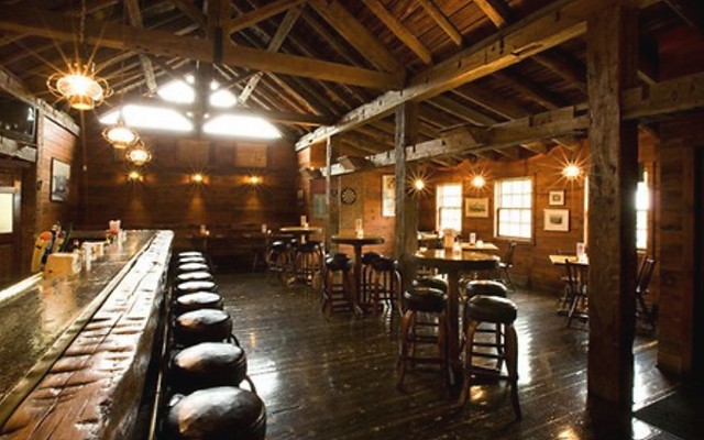 Cozy rustic bar with wooden beams and stools lined up along a counter.